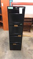 Front view of black four-drawer tall filing cabinet showing drawer pulls and overall condition.