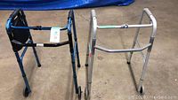 Photo showing both walkers side by side, blue and silver frames with wheels on front legs.