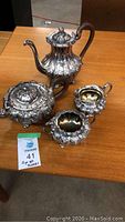 Photo showing the four-piece silver plated set of Rogers Bros, including coffee pot, teapot, cream pitcher, and sugar bowl on wooden table.