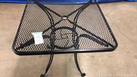 Top view of black metal mesh patio table showing square shape and center hole for umbrella.