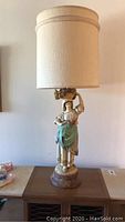 Full view of vintage porcelain table lamp with woman figurine and beige cylindrical lampshade