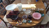 Overview of various glass pieces on table including bowls, vases, and ashtrays in multiple colors and styles.