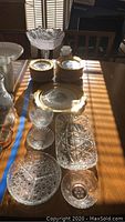 Full view of porcelain and crystal dishes including plates, bowls, serving platter and cut crystal bowls and dishes laid on wooden surface with sunlight