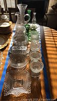 Photo showing the full set of crystal items on a wooden table including pitchers, vases, bowls, and plates under natural lighting.