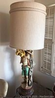 Full view of the lamp with beige cylindrical fabric shade and man figurine base