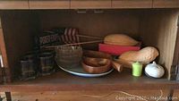 Shelf view showing almond and peanut shaped ceramic bowls, wooden segmented bowls, six glasses, glass bowls, small candle and ceramic container
