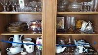 Wide view of wooden shelves showing collection of plates, glassware, teapots and candy dish on middle shelf.