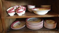 Overall display of china set including stacked dinner plates, salad plates, cups, and saucers on wooden shelving