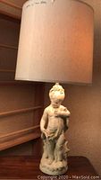 Full view of table lamp showing cream-colored cylindrical shade and toddler figurine base.