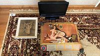 Overview of all items: television at top, framed ballet print to left, nude calendar centered on carpeted floor