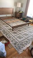 Photo showing full spread of rectangular tan floral area rug with visible fringe on the edge and partial furniture around it.