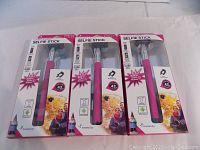 Three Travelocity pink selfie sticks in original packaging with front view of packages showing product details and branding.