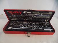 Opened red metal Husky case revealing 42-piece socket set with sockets, ratchets, and extensions arranged inside.