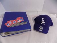 Side view of blue binder and LA Dodgers blue hat together, showing the full lot contents.