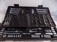 Photo of entire tool set in opened black plastic case showing upper tray with combination wrenches, pliers, screw bits, and drill bits.