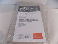 Photo of packaged new canvas drop cloth labeled 4 x 15 ft, 8 oz weight, super absorbent, washable, durable, for painting and cleaning protection.