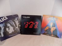 Photo showing the three Police albums arranged in a row: 'Reggatta de Blanc' on the left, 'Ghost in the Machine' in the center, and 'Zenyatta Mondatta' on the right. Covers show some wear.