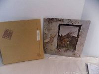 Two vinyl album covers side by side showing front and back. One cover is the famous Led Zeppelin IV with peeling wallpaper and picture of man carrying sticks, the other is a plain brown back cover with text.