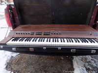 Full view of Yamaha CP-30 electric piano with woodgrain finish, keyboard, and control panel, sitting on black carrying case with handle and latches, photographed inside a vehicle.