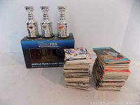 Photo showing three mini Stanley Cup trophies displaying team logos, with stacks of hockey cards behind, and Ultra Pro box underneath trophies.