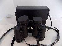 Binoculars with lens caps and carrying strap, front view showing brand and model markings.