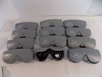Overview of 12 gray hard mountable Suntuff protective cases with one pair of sunglasses displayed in front.