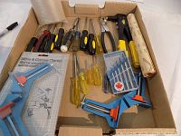Full view of all tools including screwdrivers, pliers, clamps, drill bits, and hammer in cardboard box