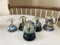 Five musical snow globes displayed on a dining table, featuring three city skylines and two lighthouse-themed bases.
