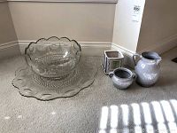 Overall view of glass punch bowl, matching plate, gray pottery pitcher, bowl, and candle holder on carpeted floor.
