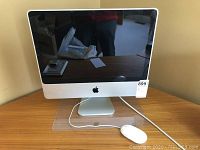 Front view of Apple iMac 20-inch computer with screen off and Apple mouse in front.