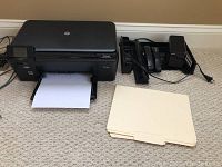HP Deskjet 5510 printer with printed paper, black with LCD screen and controls, power cable attached.