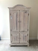 Front view of the wooden armoire cabinet showing two upper and two lower doors with carved scroll detail on the arched top.