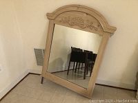 Front view of large wooden framed dresser mirror with carved top design