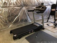 Full view of treadmill in unfinished basement showing deck, handles, and console