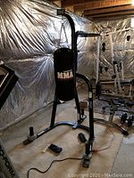 Full view of Everlast black metal two-station bag stand with Century MMA heavy bag suspended from it and gloves on floor nearby.