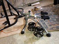 Photo of the LoveHandler exercise equipment showing metal frame, pedals, foam padded support, and mounted weight plates.