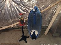 Full view of the gumball machine next to the blue skim board against a foil background, showing size and condition.