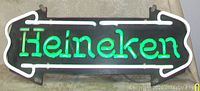 Front view lit, neon glowing green “Heineken” text with white arrow outlines against black backing