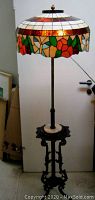Front view of entire floor lamp showing stained glass shade, metal post and ornate base with table