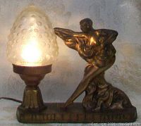 Full view of lamp lit showing frosted glass shade and bronze-toned lady sculpture on base.