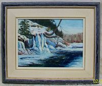 Framed oil painting showing a snowy landscape with frozen waterfall and river, signed by Peggy Ring.