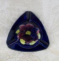 Front view of triangular Moorcroft ashtray showing deep blue color and raised floral design.