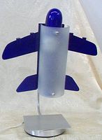 Front view of airplane form desk lamp with blue bulb cover and frosted glass shade on metal base.
