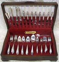Open wooden box with red velvet lining showing silverplate knives, forks, and spoons arranged within slots; front view