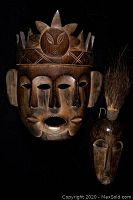 Two wooden hand-carved African Luluwa masks from Congo on black background under spotlight.