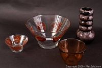 Three glass items displayed: two clear glass bowls with orange and gold leaf decoration and one purple ribbed vase.