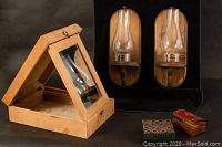 Wooden foldable campaign mirror in light wood, displayed open, with two wooden candle sconces with glass hurricane shades mounted against a black background, and two small decorative boxes in front.