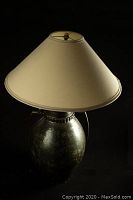 Overall view of the Mid-Century Modern table lamp with beige fabric shade and glazed stoneware base on a black background.