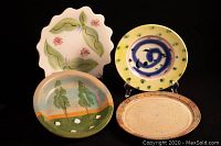 Front view of four handmade and signed pottery plates with diverse artistic designs and colors.
