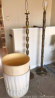 Two brass floor lamps together, one taller and one shorter, both with shades removed and placed in front. Shorter lamp shade frame is broken.